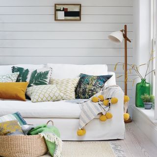 white sofa with patterned pillows against a wooden white wall with a woven basket