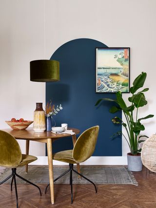 Blue painted DIY wall arch in dining space with olive green velour chairs, artwork and house plants