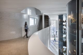 Circular viewing gallery, white brick walls, curved white walls, stairwell, blurred female visitor, centre piece display towers containing ornaments, glass front foyet in the distance
