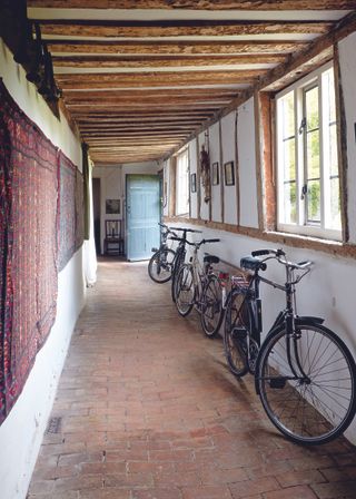 Original tiled floor with undulating surface in the hallway of an older home, with wood beams in the ceiling and bicycles to the right of the hallway