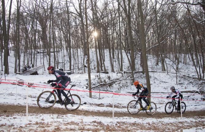 The winter sun peeks through the trees as riders head back towards the finish