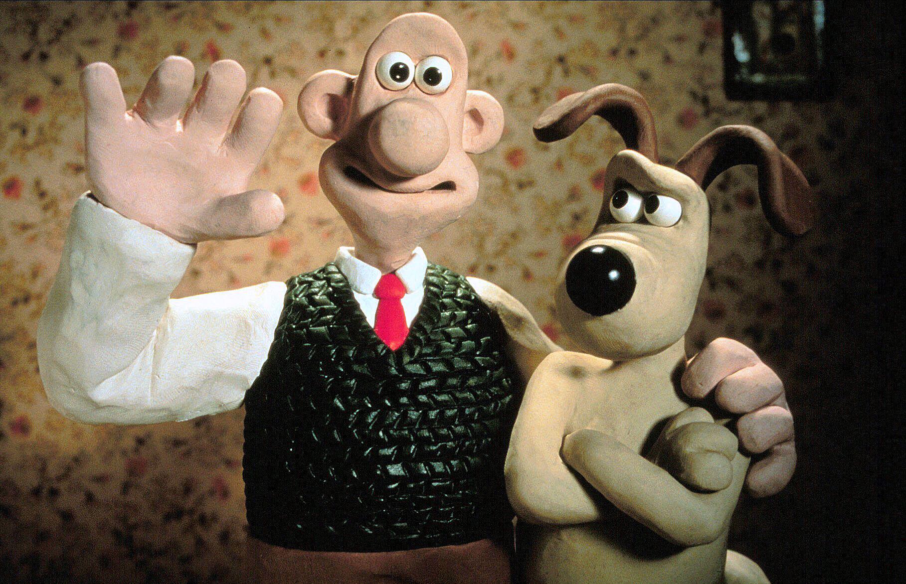 Wallace, in a green knitted vest and red tie, waves cheerfully while Gromit stands beside him with folded arms, looking unimpressed.