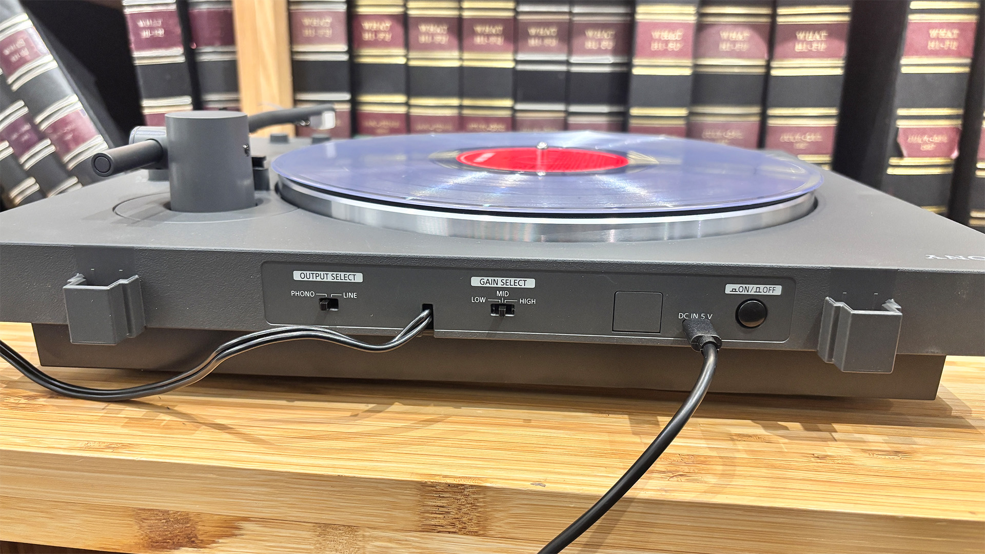 Sony PS-LX3BT Bluetooth turntable on wooden hi-fi rack in front of bookcase, rear of turntable showing connections