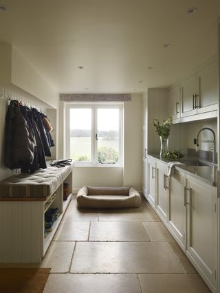A utility room in neutral tones with coat hooks and a seat to one side and a sink to the other