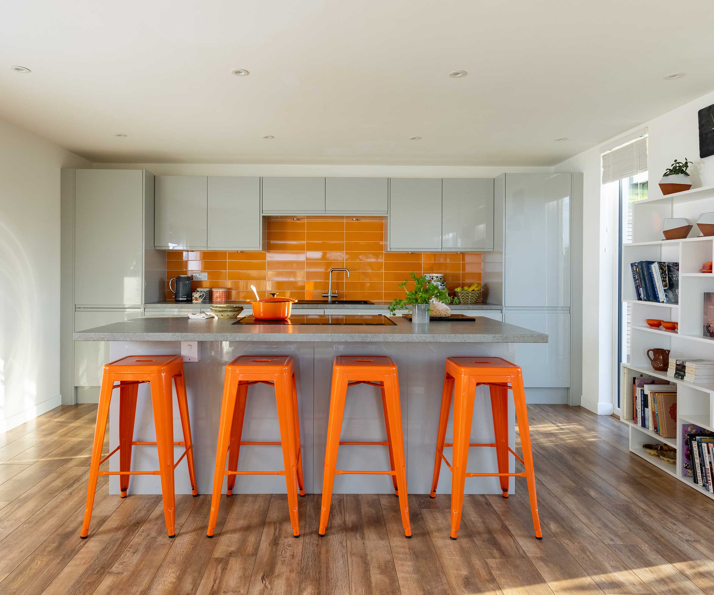 Modern kitchen with pale units, wooden flooring and bright orange wall tiles and bar stools