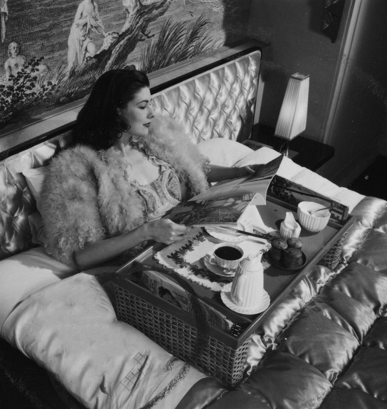 Photograph by Zoltan Glass of a model wearing a mohair or feather bed jacket, reading a magazine, with her morning coffee on a tray.