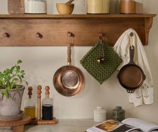 Off white marble counter with wooden accessories and a peg shelf with copper pans and crochet/linens hanging