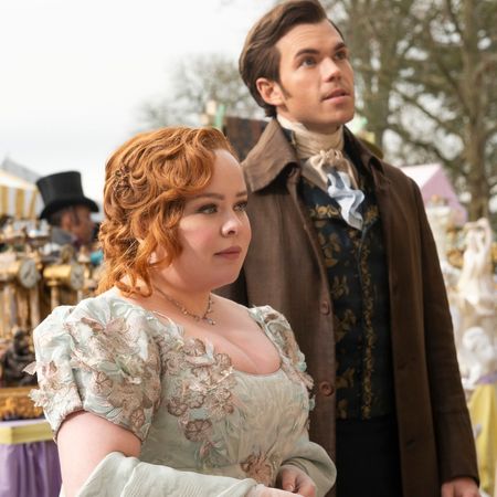 nicola coughlan as penelope featherington and luke newton as colin bridgerton, standing apart from the crowd at an outdoor event, in 'bridgerton' season 3