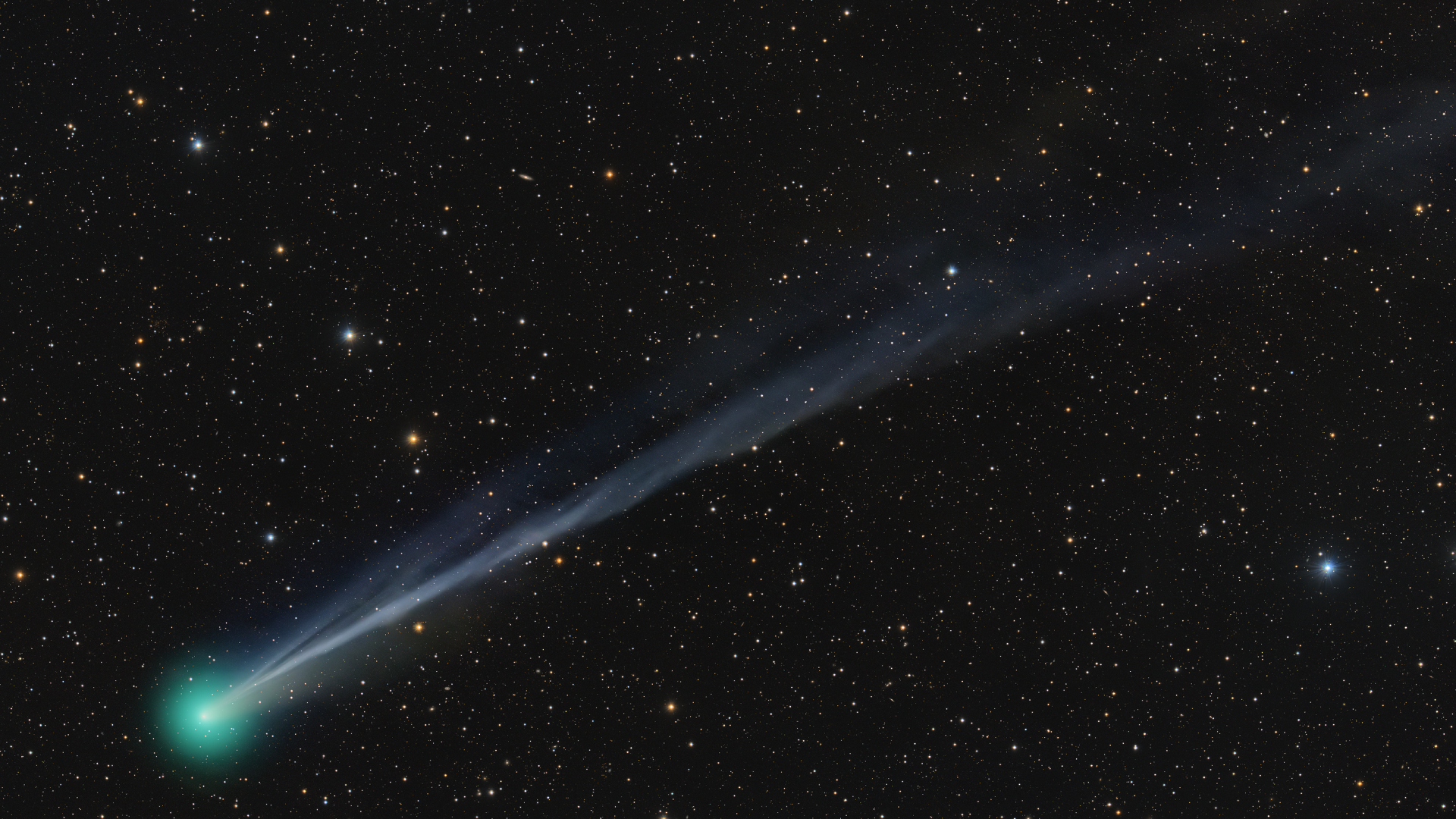 A bright green comet is pictured to the bottom left of a starfield against a black sky, with a long tail extending to the upper right of the screen.
