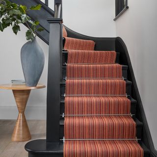 Oak wood staircase with red stripey runner in white hallway