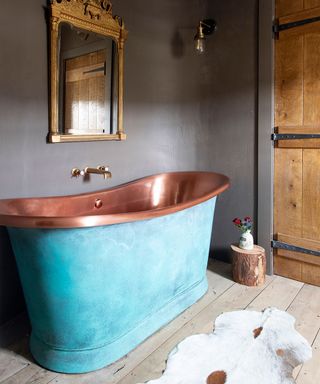 A grey bathroom with gold mirror and copper bath tub by luxury bathroom designers Perrin & Rowe.