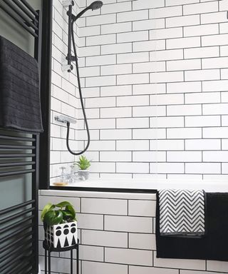 A contemporary bathroom with shower over bath setup with white metro tile wall decor and black modern heated towel rail