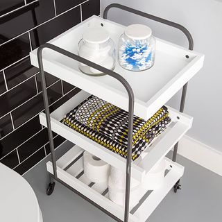 bathroom with grey tiled walls and wheeled shelf trolley