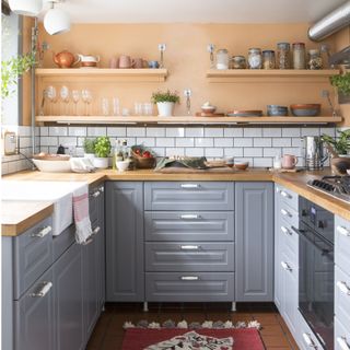 kitchen with a peach wall, wooden shelving and wooden worktops and grey cabinets