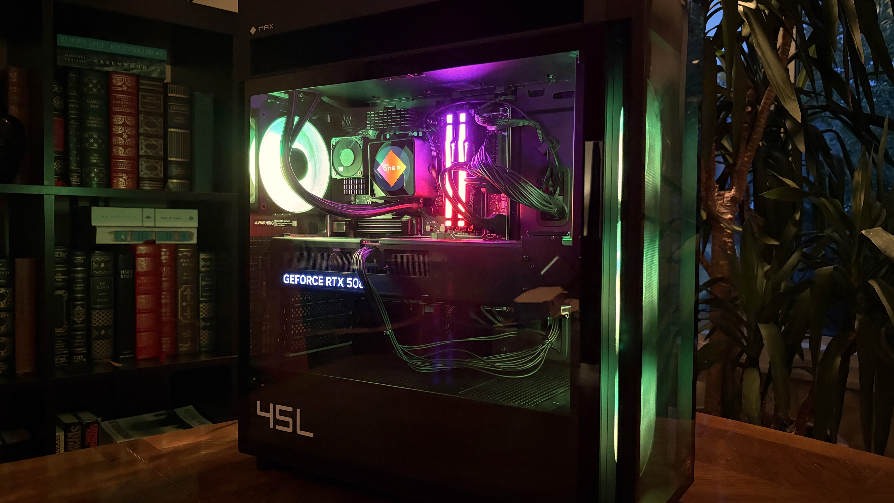 A modern HP Omen Max 45L computer tower with a glass side panel showcasing colorful internal components, including a glowing cooling fan and RAM, is set against a backdrop of bookshelves.