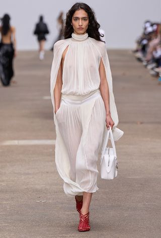 Woven shoe trend shown in Stella McCartney's spring 2025 runway show with a model wearing a white draped gown with a white bowler bag and red cage woven heels