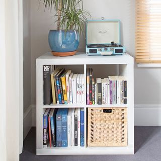 white storage unit with books and a basket and plant and record player on top
