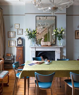 dining room with gray walls, vintage mirror, marble fireplace, table with green tablecloth and blue leather chairs