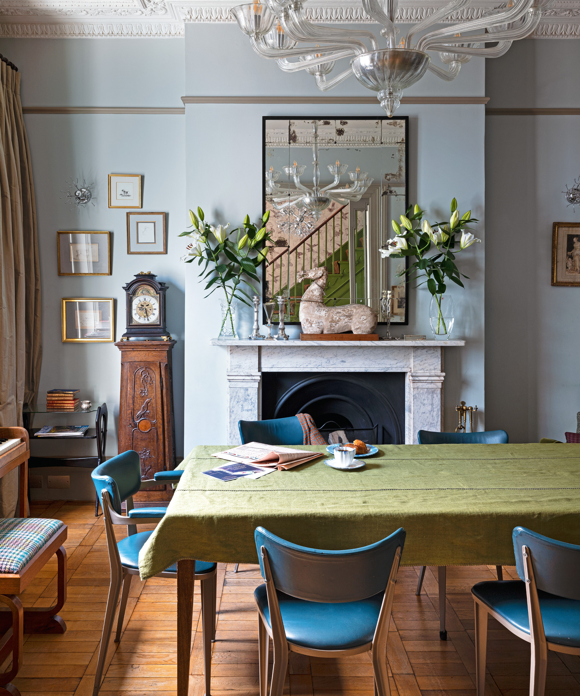 comedor con paredes grises, espejo antiguo, chimenea de mármol, mesa con mantel verde y sillas de cuero azul