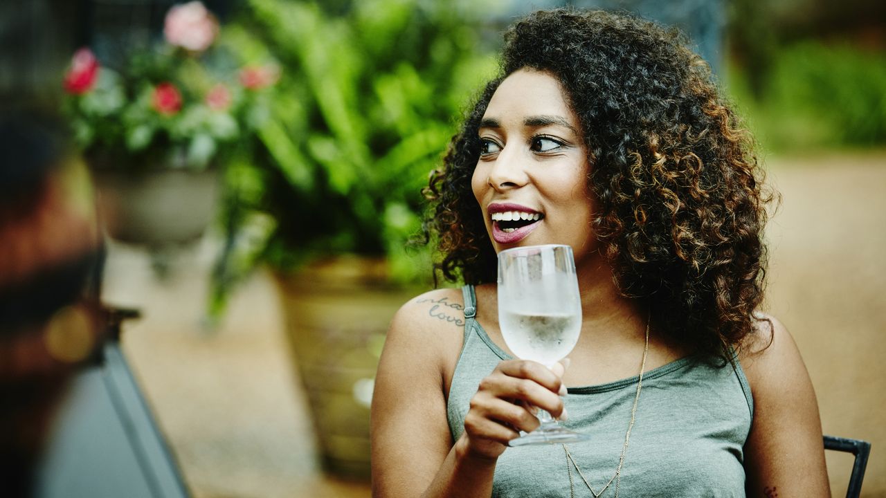 Person having a conversation outdoors, holding a glass of white wine