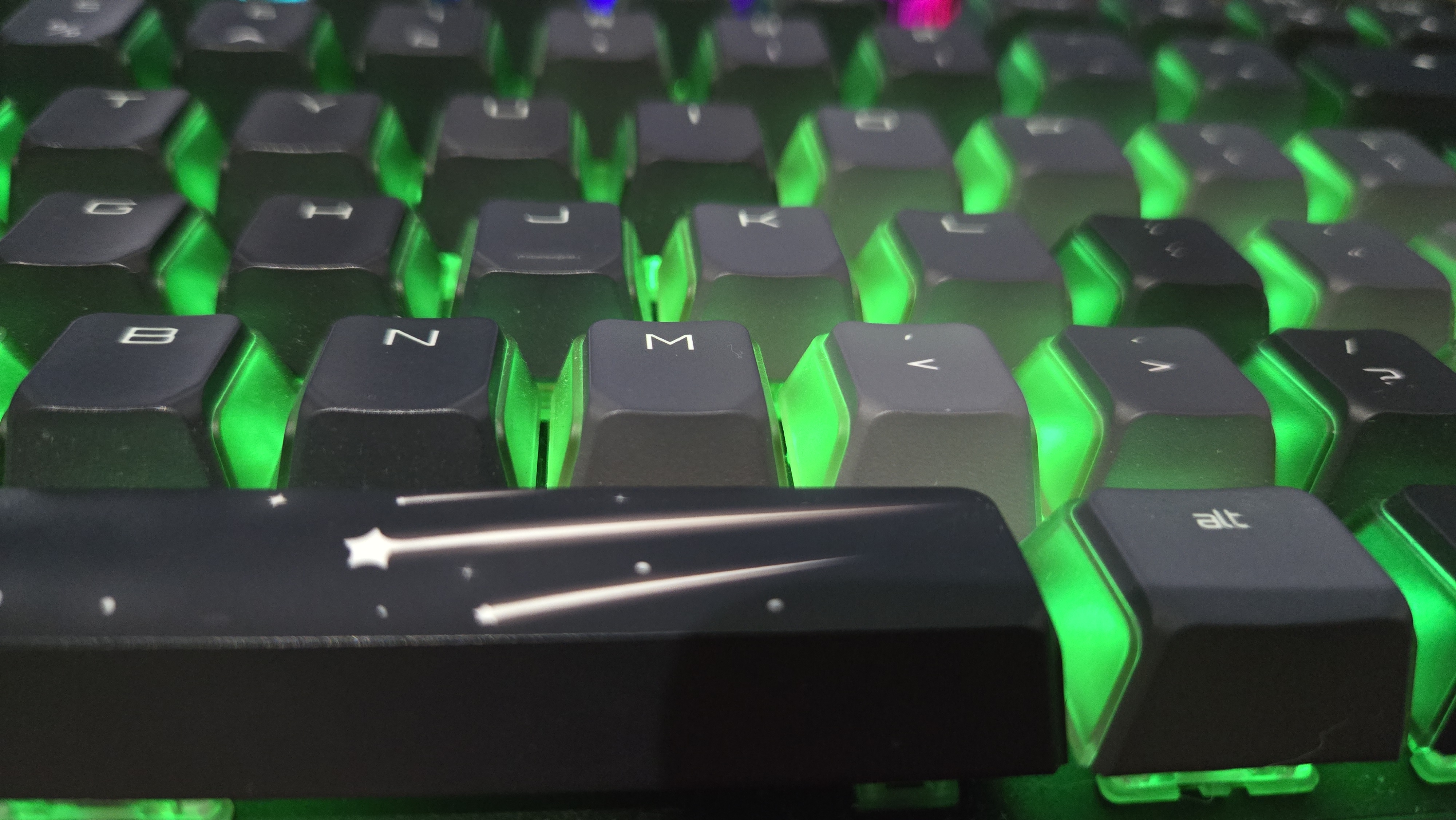 A close up on the space bar of the Cherry MX 8.2 Wireless Xaga gaming keyboard. The RGB lights are on. The space bar key features an opaque shooting star design that the RGB lights cannot shine through.