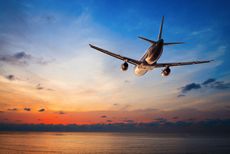 An airplane flies into a sunset sky.