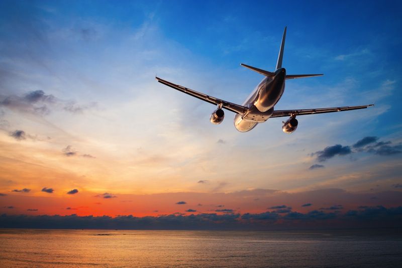 An airplane flies into a sunset sky.