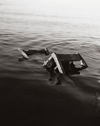 black and white photograph of a wooden chair floating in water