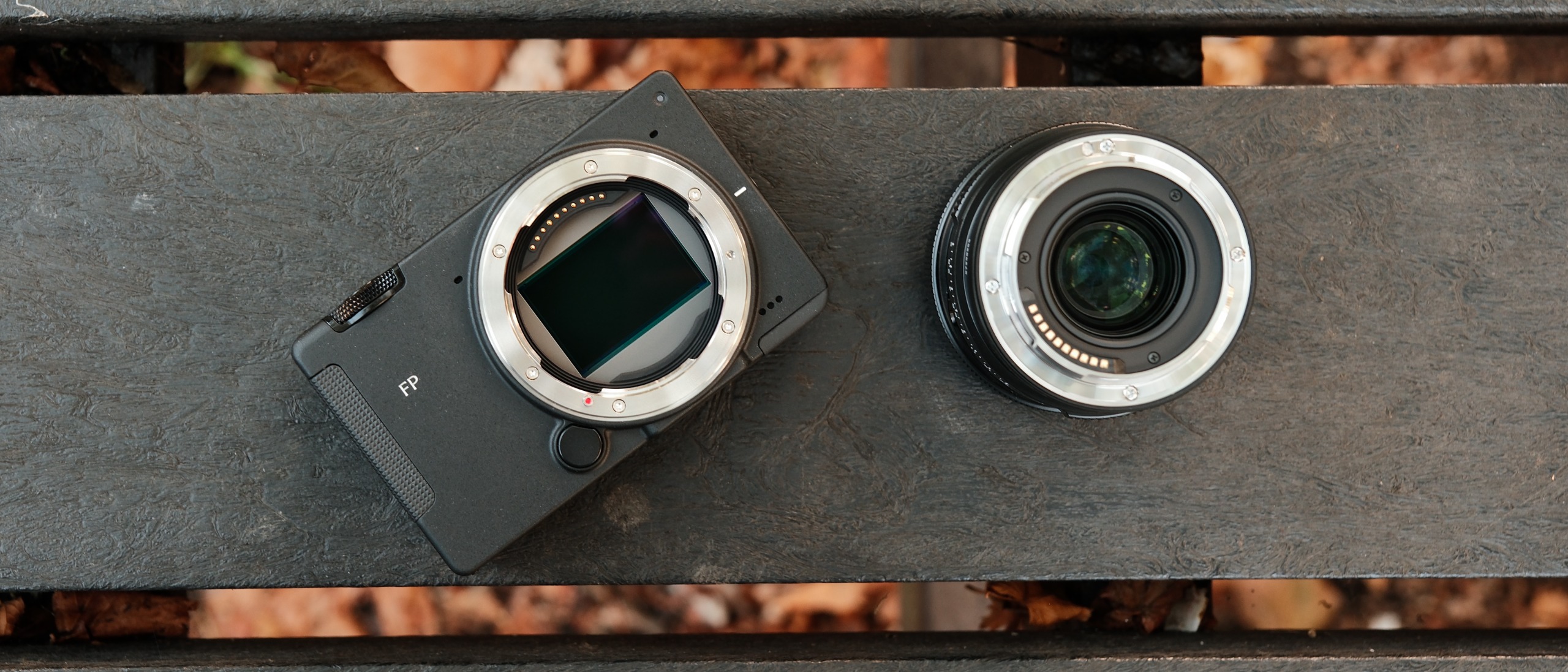 Sigma FP2 camera body and 50mm lens placed side by side on a wooden bench.