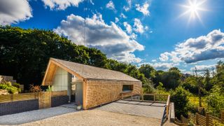 exterior of one of storey of eco house clad in timber shingles with large gravel area outside and large trees along rear of property