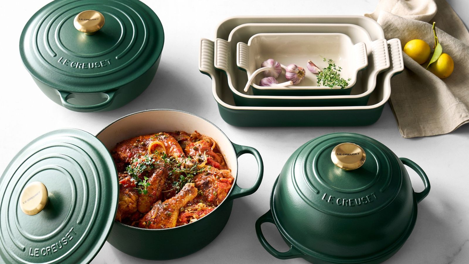 The Le Creuset enameled cast iron collection in deep Foret green, on a marble counter. 