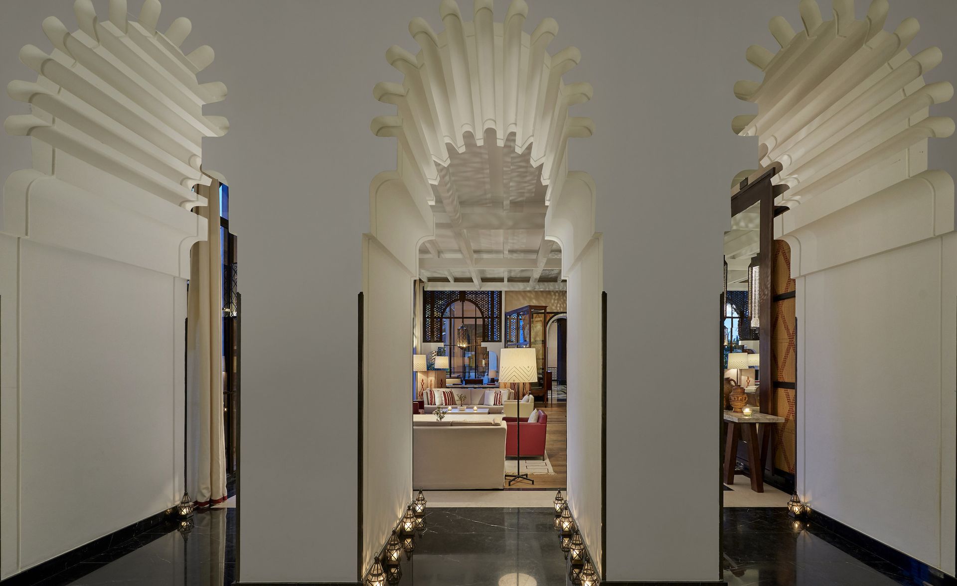 A hotel sitting area with sofas, floor lamps and large arched doorways.