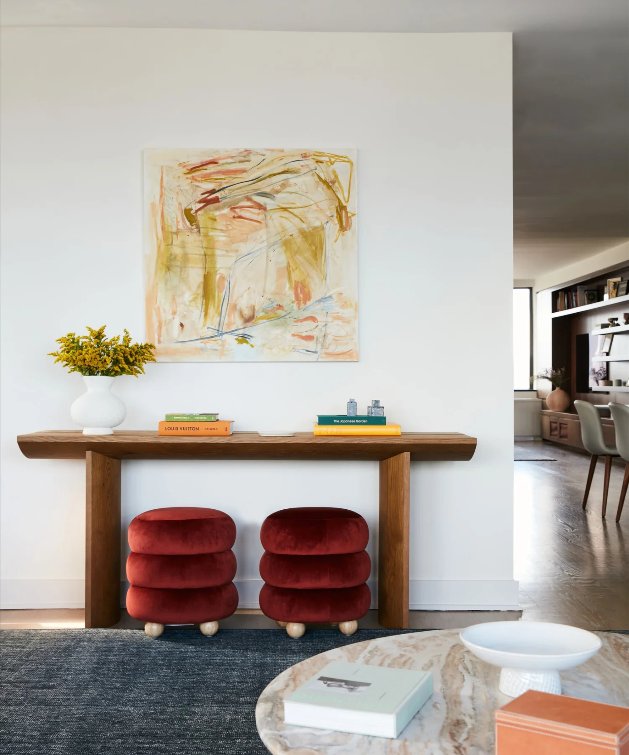 a console table with two red velvet stools underneath, decor on top, and an abstract yellow painting on the wall