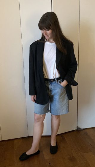 senior fashion editor Halie LeSavage standing in front of her closet wearing an oversize blazer and the jorts trend with mesh flats