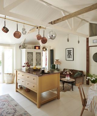 A white kitchen with an island with yellow shaker cabinet doors and copper pans hanging from the ceiling