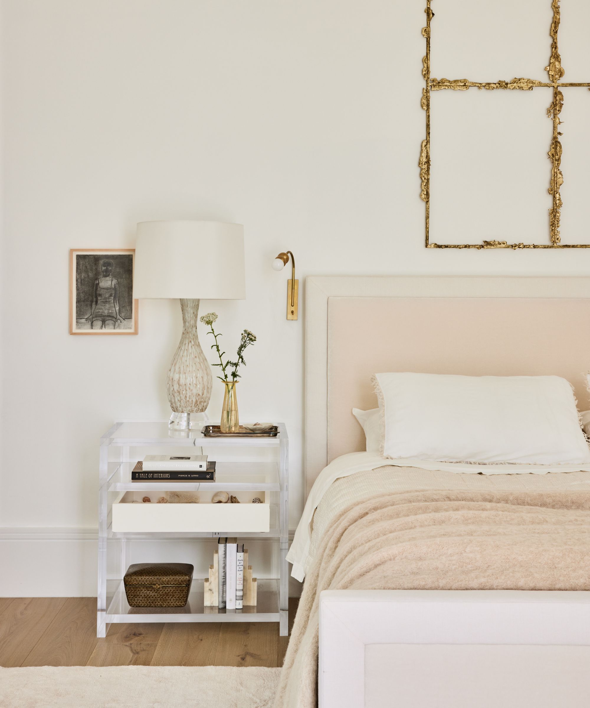 bedroom with warm white walls blush upholstered bed and throw and bronze sculpture above
