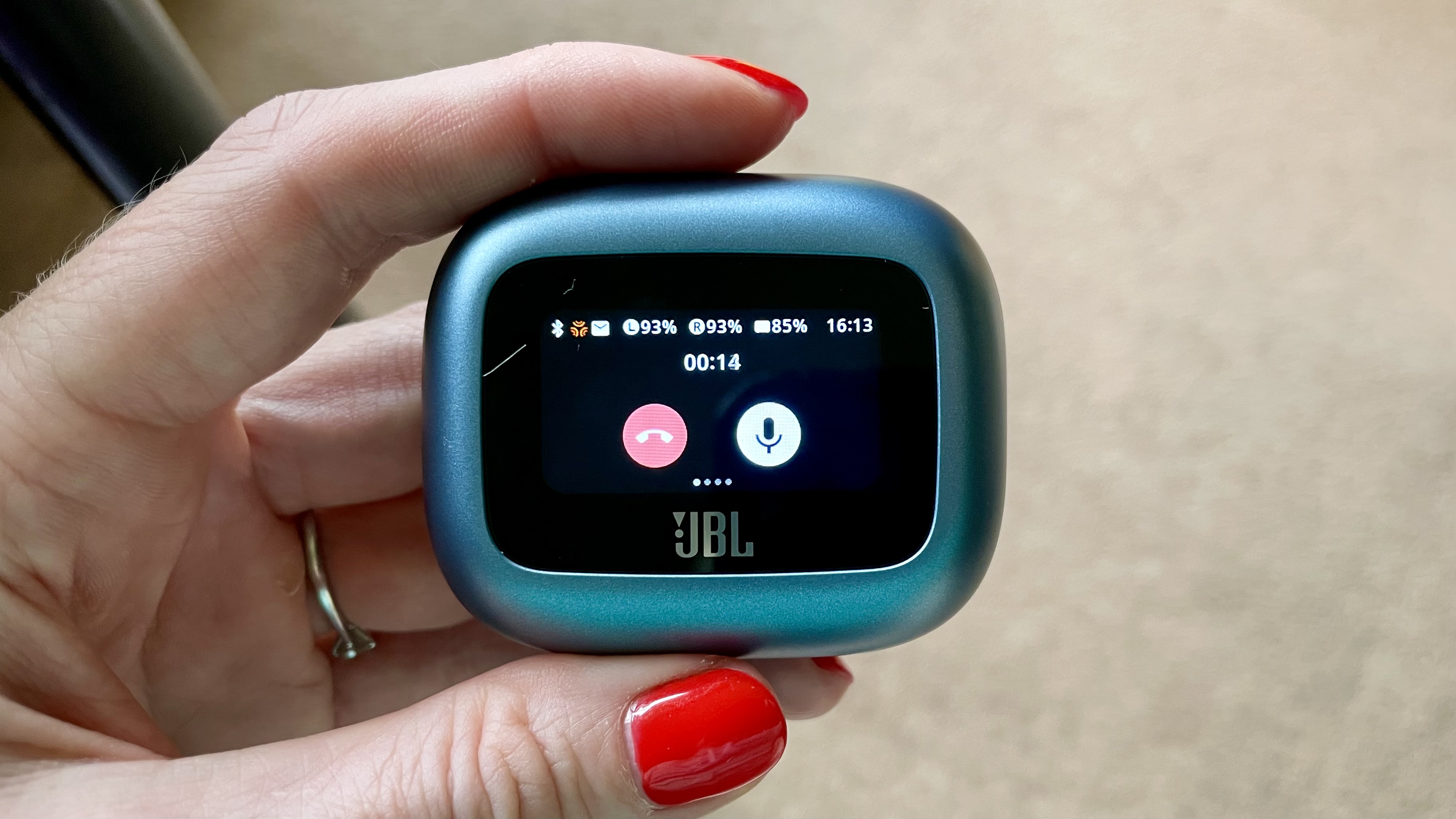 JBL Live Beam 3, showing an incoming call, case held in a hand with red fingernails
