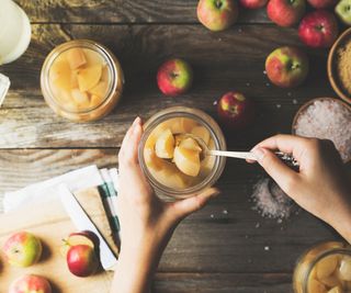 Making apple cider vinegar - a hand adding apples to a jar making apple cider vinegar surround by ingredients