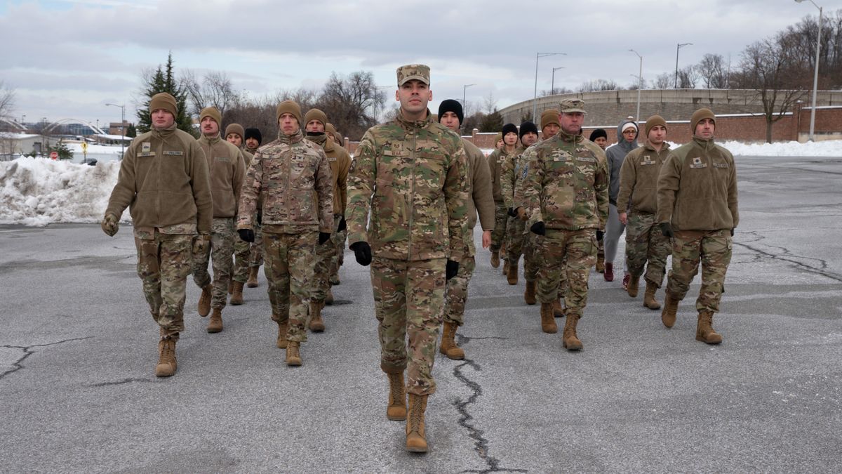 a group of military personnel in green camouflage fatigues practices marching in a snowy parking lot