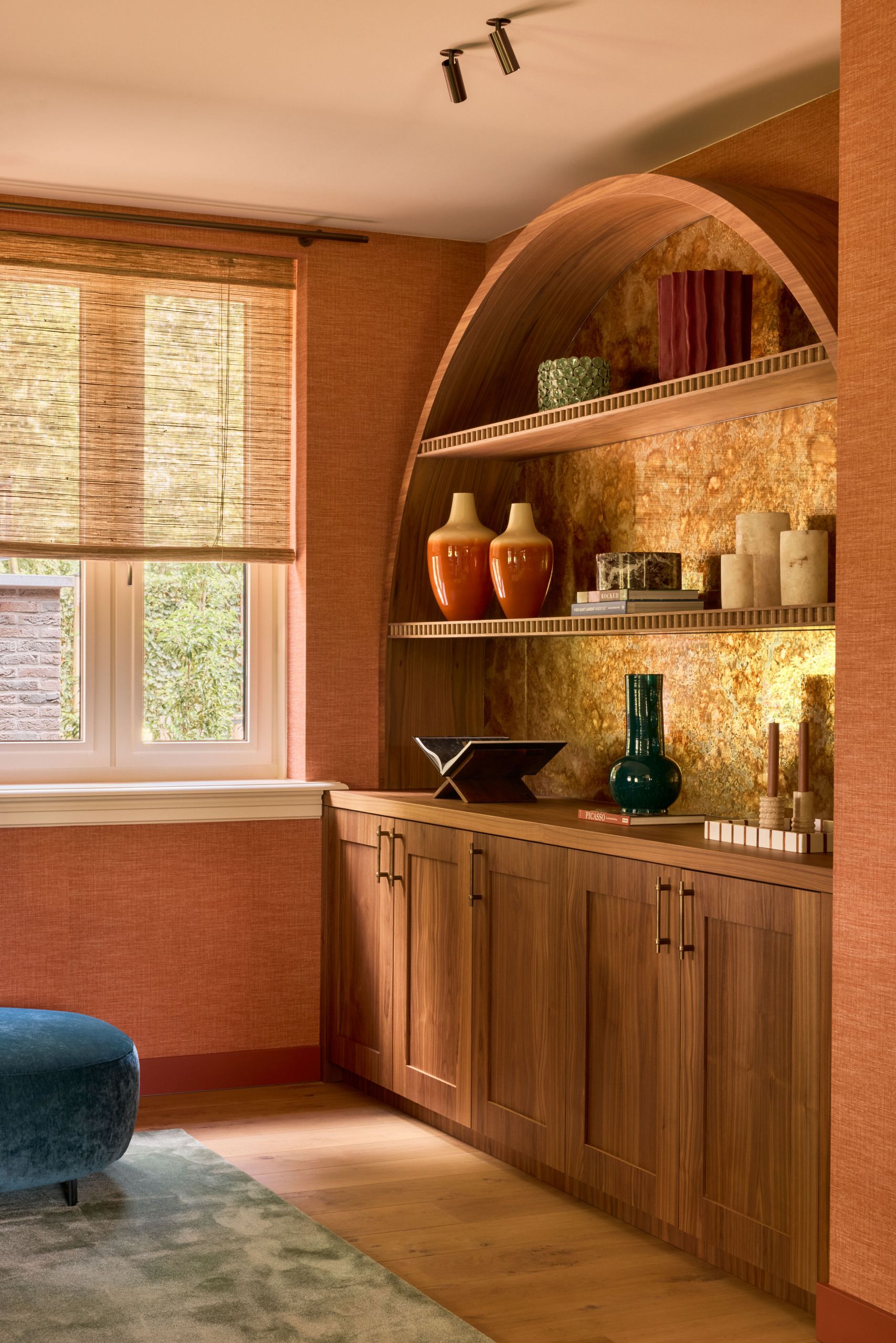 Image of a bright coral room with an arched built-in shelving unit that has a golden back splash.