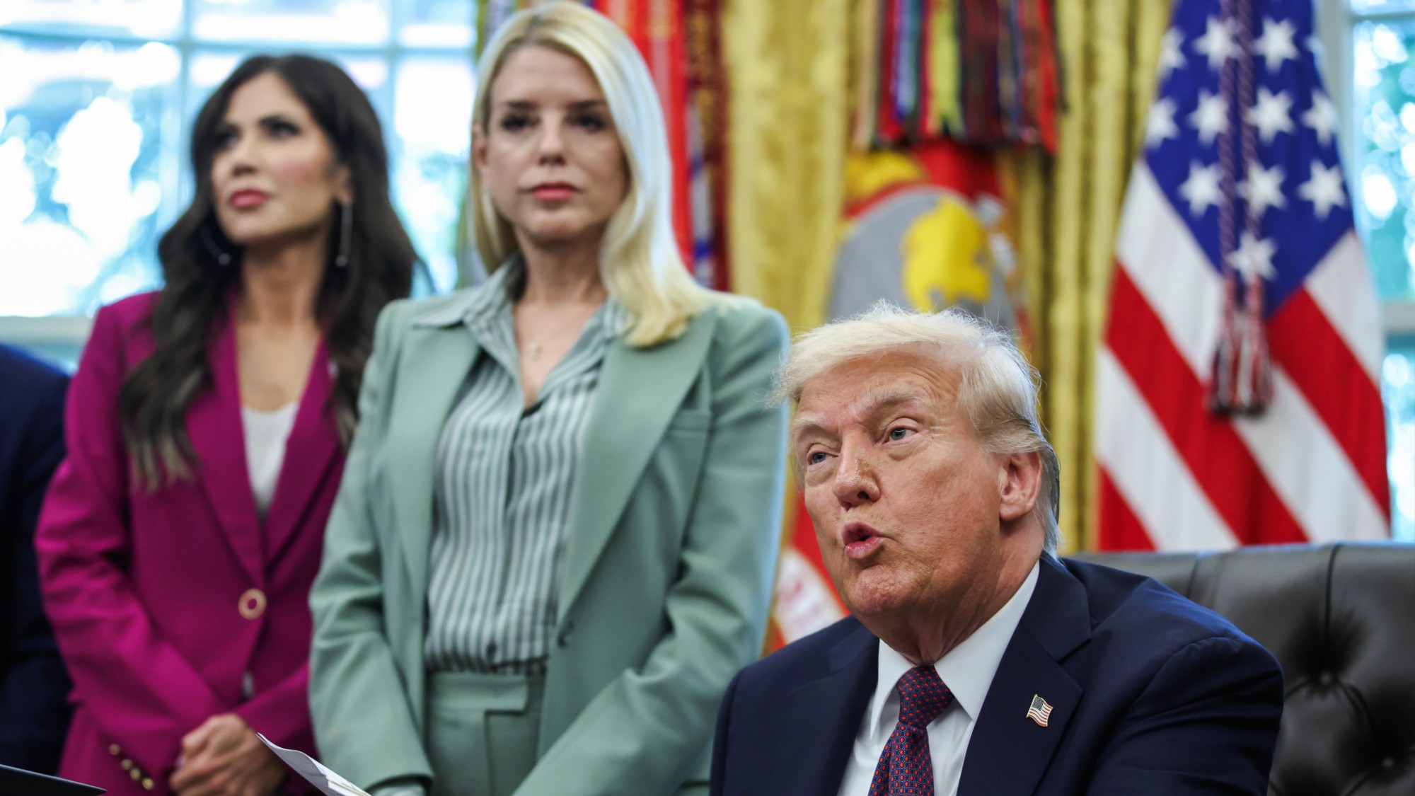 Kristi Noem and Pam Bondi stand behind President Trump in the Oval Office