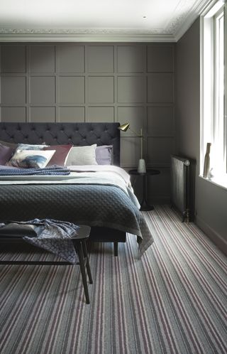 Bedroom with bed, striped carpet and gray paneled wall