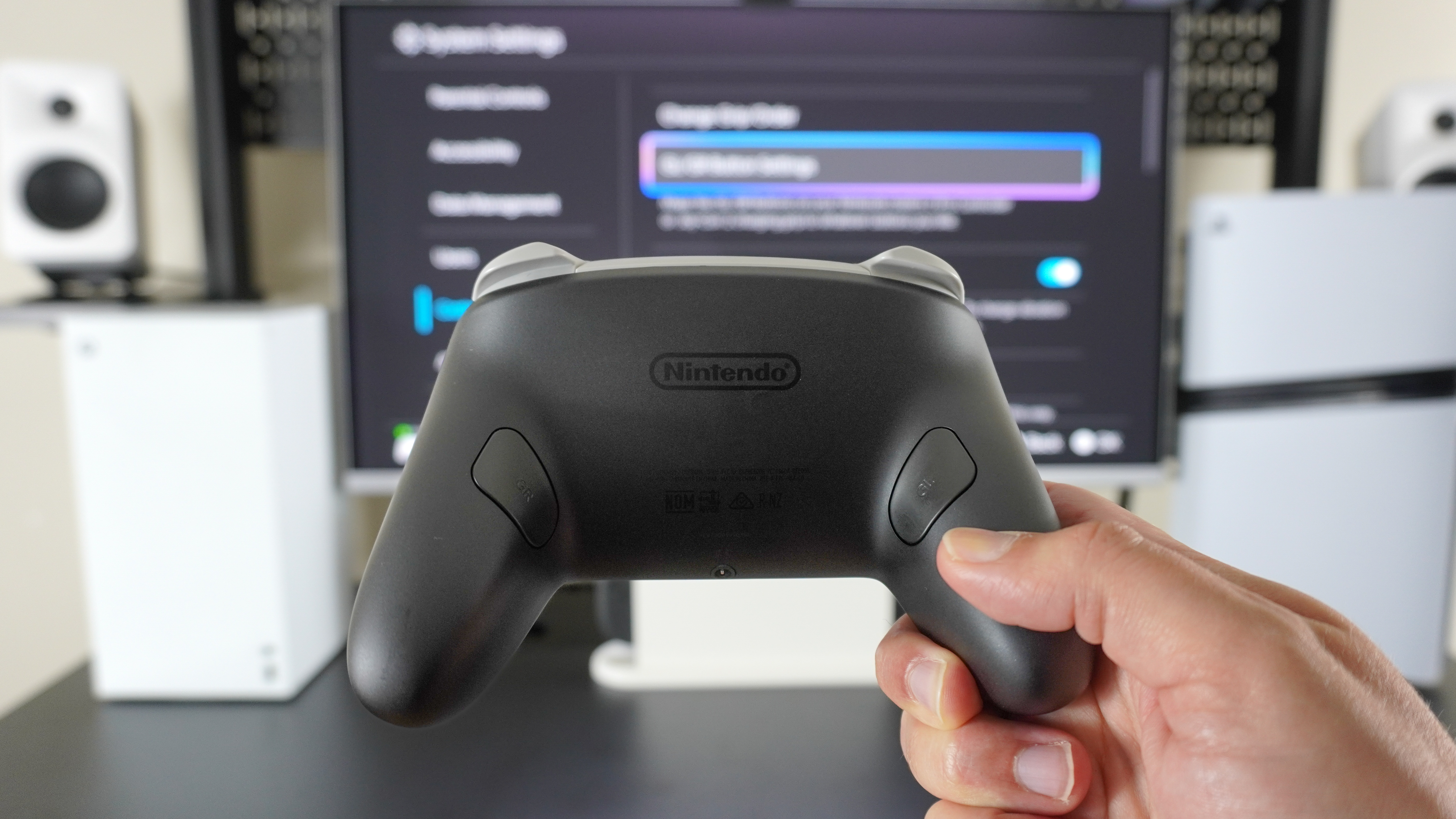 A person holding up a Nintendo Switch 2 Pro Controller in front of a desk with its remappable back buttons clearly visible
