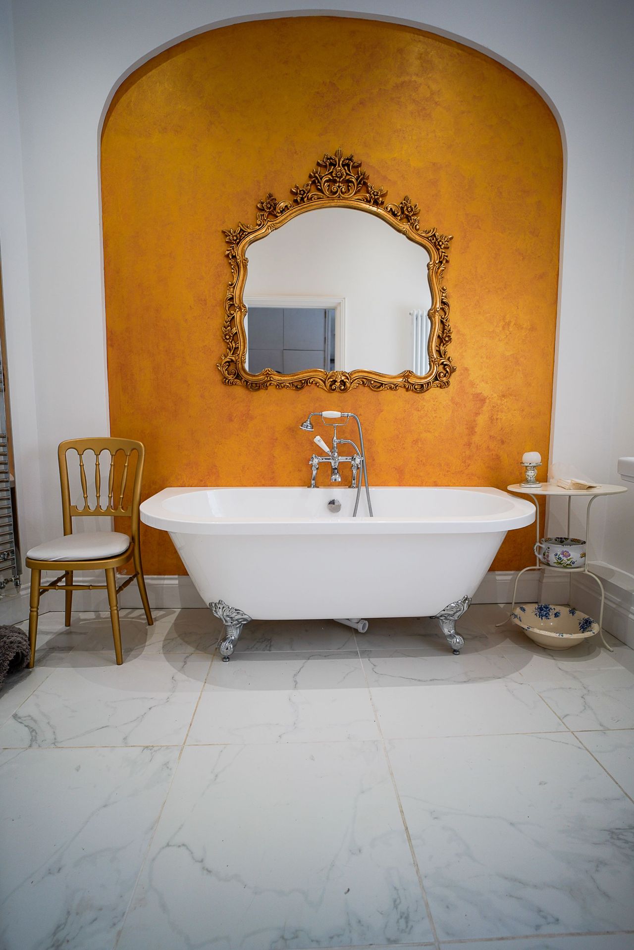 A large rolltop bathtub with an orange feature wall behind