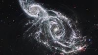 A deep space image showing the white gas and stars forming two spiral galaxies next to each other, stretching from the bottom right to top left of the image. 