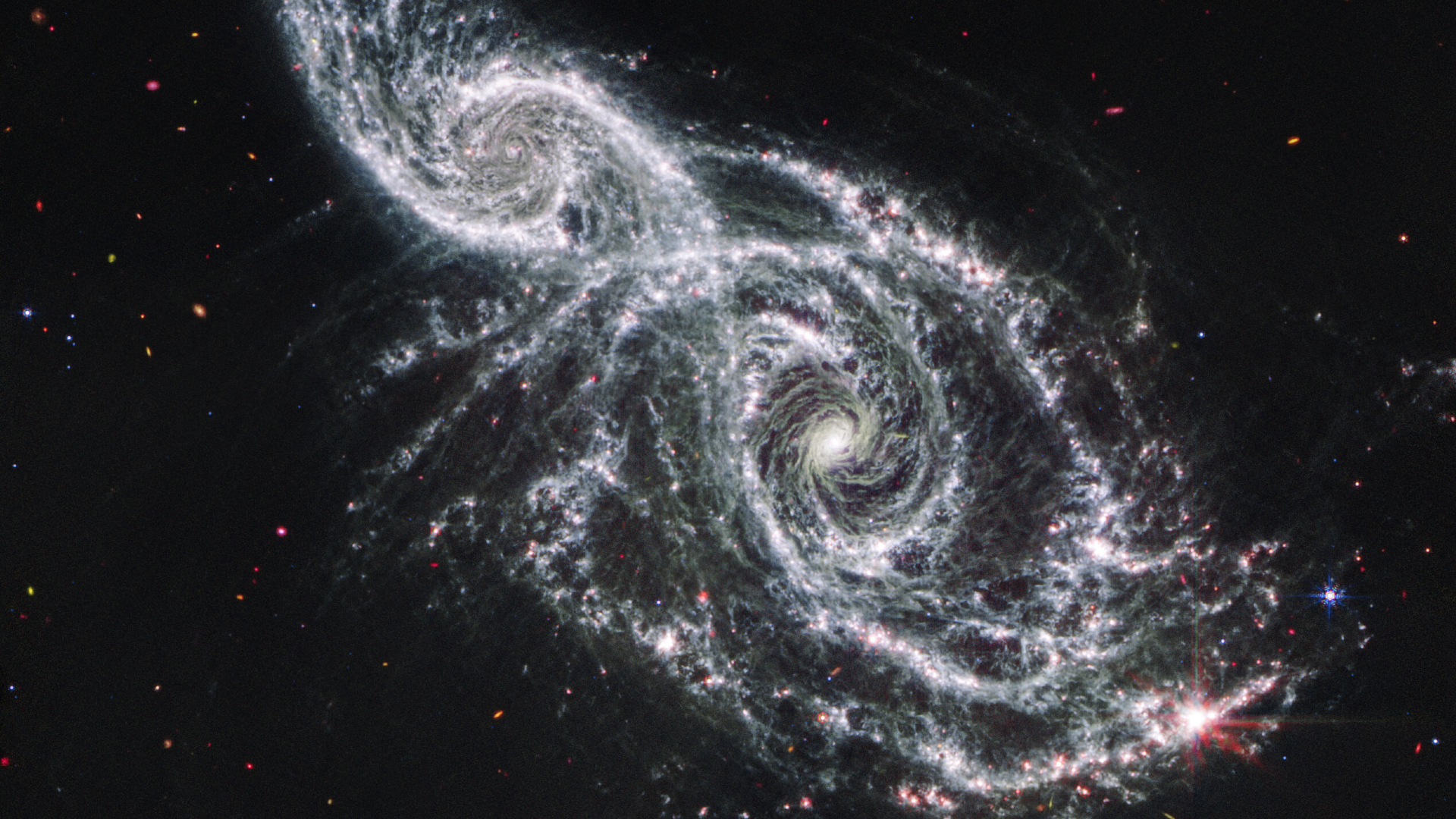 A deep space image showing the white gas and stars forming two spiral galaxies next to each other, stretching from the bottom right to top left of the image. 