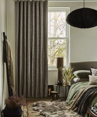 A bedroom with dark curtains, faux fur rug and bed