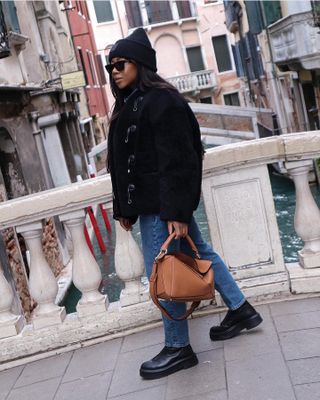 A woman wearing skinny jeans with lug sole boots, a loewe brown bag, and black fur jacket.