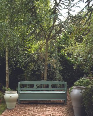 A herringbone brick pattern and green painted storage bench with trees behind.