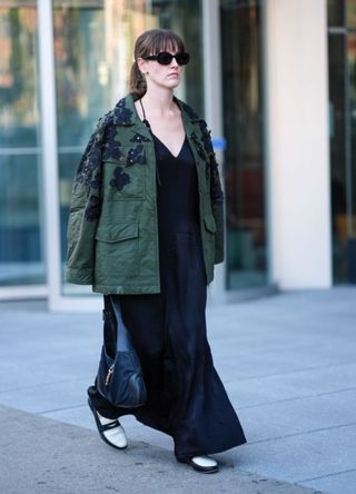 A woman in New York wearing sunglasses, a green denim oversized jacket with floral details and a black low neck dress